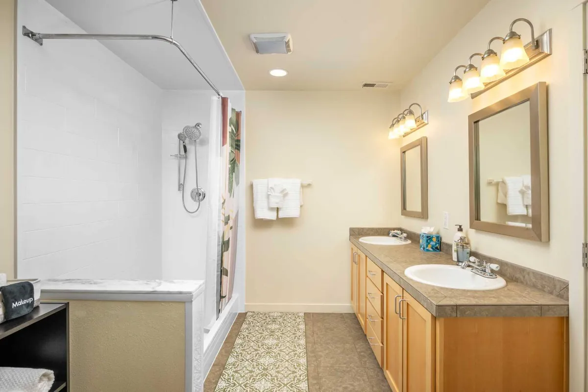 A bright, modern en-suite bathroom showcasing double vanity sinks, a walk-in shower, decorative floor tiles, and large mirrors. The spa-like atmosphere is accentuated by clean lines and inviting lighting.