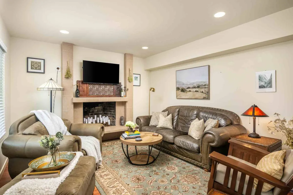 A cozy living room with a fireplace, plush sofas, coffee table, and tasteful artwork. The atmosphere is warm and designed for relaxation, reading, or gathering with friends and family.