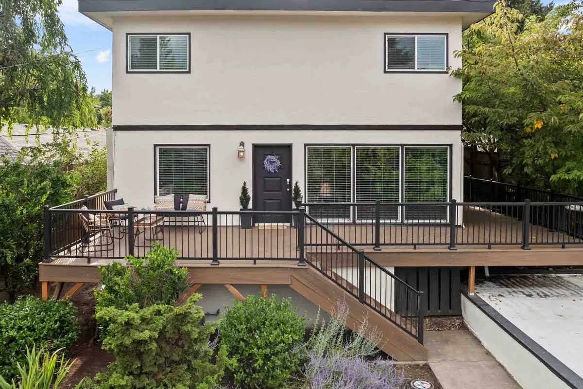 This image showcases the home's front deck with ample seating, a welcoming facade, large windows, and lush landscaping. The deck is bathed in natural light and surrounded by greenery, making it an ideal spot for morning coffee or relaxing amidst the quiet neighborhood.