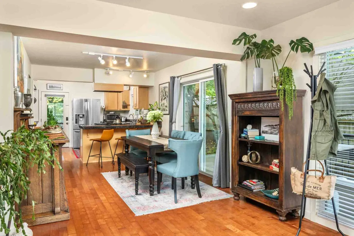 The image captures an inviting, light-filled dining area featuring a spacious table surrounded by comfortable chairs, with a stylish bookshelf lining one wall. Large windows bathe the room in natural sunlight, creating a relaxing atmosphere ideal for gathering, dining, or quietly enjoying a book.
